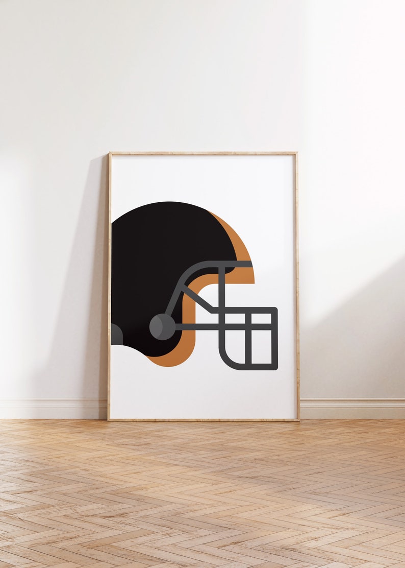 Op de afbeelding: Een zwarte en bruine voetbalhelm met een grijs gezichtsmasker. De helm staat op een witte achtergrond.
