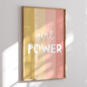 May include: A framed print with a yellow, orange, and pink striped background. The text "girl power" is written in white on the print.