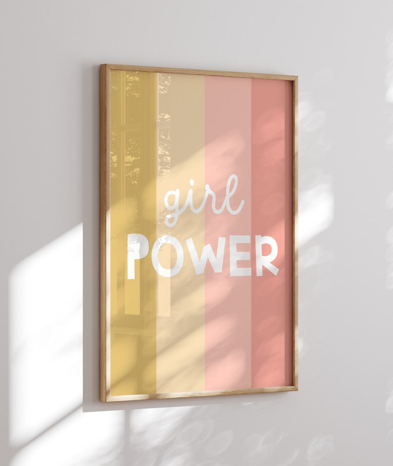 May include: A framed print with a yellow, orange, and pink striped background. The text "girl power" is written in white on the print.