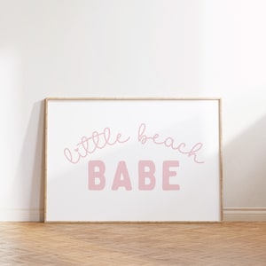 May include: A framed print with the text "little beach BABE" in pink lettering on a white background.