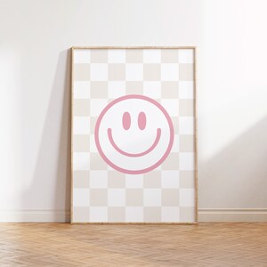 Op de afbeelding: Een ingelijst print met een roze smiley op een beige en witte geruite achtergrond.