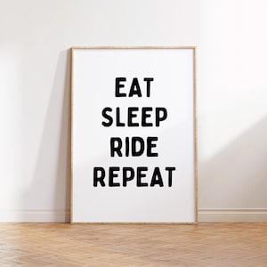 Op de afbeelding: Een ingelijst print met de tekst "EAT SLEEP RIDE REPEAT" in zwarte vetgedrukte letters op een witte achtergrond.