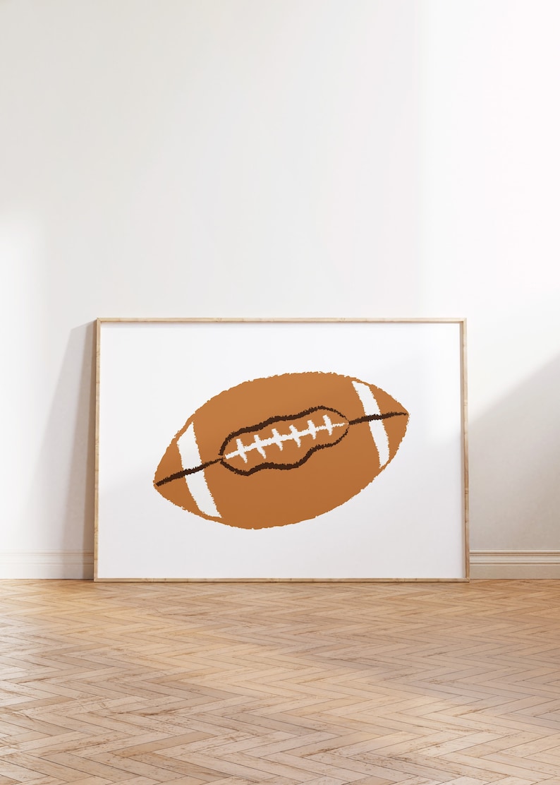 Op de afbeelding: Een ingelijst afdruk van een bruine en witte voetbal op een witte achtergrond. De voetbal is getekend in een eenvoudige, cartoonachtige stijl.