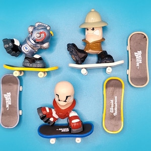 Pode incluir: Cinco brinquedos de fingerboard com diferentes personagens e designs. Cada brinquedo está em um skate em miniatura com as palavras "Tech Deck" impressas na parte inferior. Os personagens incluem um robô, um homem usando um chapéu de safári e uma figura vermelha e branca.