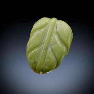 May include: A carved jade leaf pendant. The leaf is a light green color with detailed veining and a smooth, polished surface. The pendant is a naturalistic representation of a leaf.