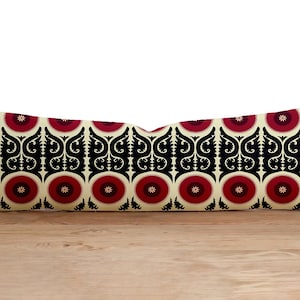 Könnte beinhalten: Ein langes rechteckiges Kissen mit cremefarbenem Hintergrund und einem geometrischen Muster in Schwarz und Rot. Das Muster zeigt sich in sich wiederholenden Kreisen mit roter Mitte und schwarzen floralen Designs.