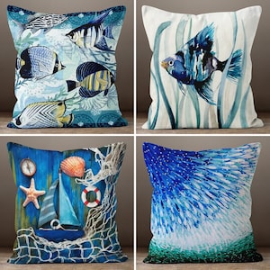 May include: Four decorative throw pillows with a nautical theme. The pillows feature blue, green and white colours with various fish designs. One pillow has a blue and white fish design on a white background. Another pillow has a blue and green fish design on a white background. The third pillow has a blue and white fish design on a blue background. The fourth pillow has a blue and white fish design on a blue background with a net and a seashell.