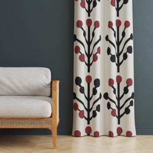 Puede incluir: Cortina color crema con un patrón repetido de ramas negras estilizadas y formas circulares rojas y negras. La cortina cuelga frente a una pared azul verdoso oscuro, junto a un sofá gris claro con marco de madera.