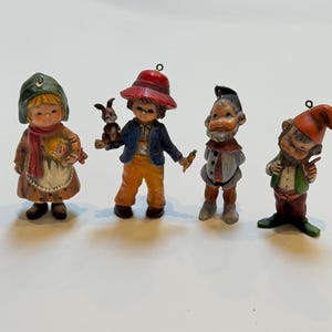 Puede incluir: Cuatro figuras de cerámica vintage. Una niña con gorro y delantal, un niño con un conejo, un hombre con una zanahoria y un gnomo. Cada figura está pintada con detalles y colores vibrantes, para coleccionistas.