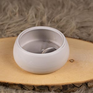 Könnte beinhalten: Eine weiße Keramik Schale mit runder Form und glatter, matter Oberfläche. Die Schale ist leer und steht auf einer Holzoberfläche.