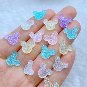 Puede incluir: Surtido de adornos de resina con forma de cabeza de ratón con purpurina de colores. Los adornos son en tonos azules, morados, rosas y amarillos.