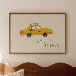 May include: A framed print featuring a yellow taxi cab illustration with the words "NYC PLEASE" in black. The artwork is set against a beige background and framed in a wooden frame. The image is displayed above a bed with striped bedding.