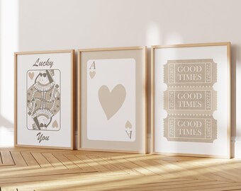 May include: Three framed prints with a beige background. The left print features a queen of hearts playing card with the text "Lucky You". The middle print features a beige heart playing card with the letter "A" in the corners. The right print features three tickets with the text "Good Times" repeated.