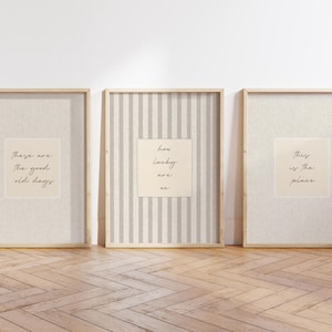 Może przedstawiać: Trzy oprawione grafiki ścienne w jasnych drewnianych ramach. Lewa grafika zawiera napis 'These are the good old days', środkowa ma pionowe paski i napis 'how lucky are we', a prawa grafika zawiera napis 'this is the place'.