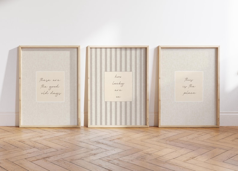 Może przedstawiać: Trzy oprawione grafiki ścienne w jasnych drewnianych ramach. Lewa grafika zawiera napis 'These are the good old days', środkowa ma pionowe paski i napis 'how lucky are we', a prawa grafika zawiera napis 'this is the place'.