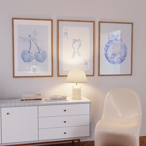 Peut inclure: Trois impressions d'art encadrées avec des motifs aquarelles bleu clair. L'une représente des cerises avec un nœud, une autre un as de pique avec des nœuds et la troisième une boule disco avec un nœud. Les cadres sont en bois.