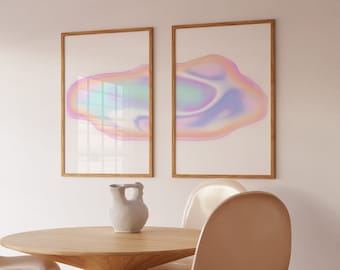May include: Two framed abstract art prints with iridescent pink, blue, and green colors. The prints are hanging on a white wall above a wooden table with two light pink chairs.