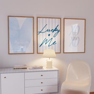 Könnte beinhalten: Drei gerahmte Kunstdrucke mit hellblauen und weißen Designs. Ein Druck sagt "This is the place", ein anderer "Lucky Me" und der dritte "XO XO". Die Drucke werden über einem weißen Schrank mit einer Lampe angezeigt.