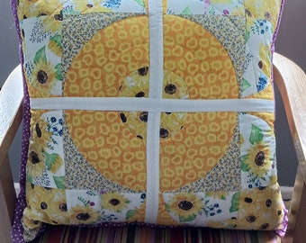 Peut inclure: Un fauteuil rayé avec un coussin à motif de tournesols jaunes. Le coussin est fait de carrés de tissu cousus ensemble en un motif circulaire.