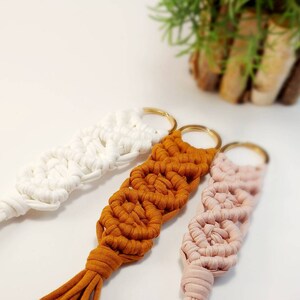 Peut inclure: Trois porte-clés en macramé faits à la main avec des anneaux dorés. Les porte-clés sont faits avec du cordon blanc, orange et rose.