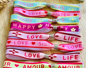Op de afbeelding: Een set kleurrijke vriendschapsarmbanden met verschillende zinnen, waaronder "Good Vibes", "Love Sister", "Happy", "Love" en "Life".