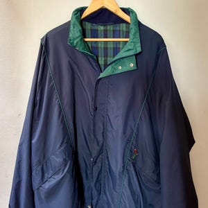 Op de afbeelding: Een marineblauw windjack met een groen en blauw geruite voering, een hoge kraag, lange mouwen met elastische boorden, een sluiting met drukknopen aan de voorzijde en twee zijzakken met een klein geborduurd golferlogo aan de linkerzijde.