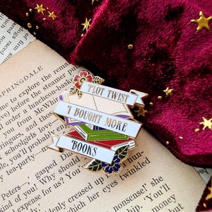 May include: Gold enamel pin with a stack of books and the text "I bought more books" and "Plot Twist".