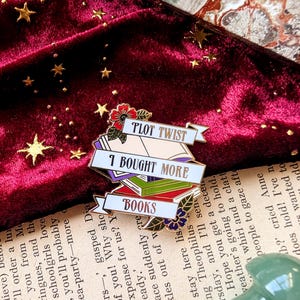 May include: Gold-tone enamel pin with a stack of colorful books, a banner that reads "Plot Twist: I Bought More Books", and a floral design.