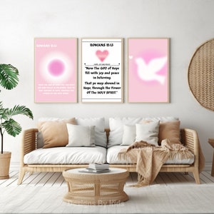 May include: Three pink and white framed prints with bible verses from Romans 15:13. The first print features a pink circle, the second print features a pink heart, and the third print features a white dove.