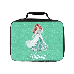 May include: A green glitter lunch bag with a black handle and zipper. The bag features a cartoon image of Ariel from The Little Mermaid and the name "Kaycey" printed on the front.