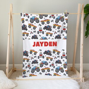 May include: White personalized blanket with a red monster truck pattern and the name "JAYDEN" printed in red.