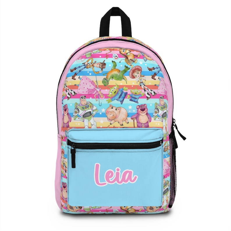 May include: A pink and blue backpack with a colorful pattern of Toy Story characters. The backpack has a large front pocket with the name "Leia" written in pink.