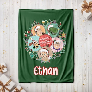 May include: A green Christmas blanket featuring cartoon characters in ornaments, with the text "Merry Christmas" and the name "Ethan" in red. The blanket has a festive design with Christmas lights and ornaments.