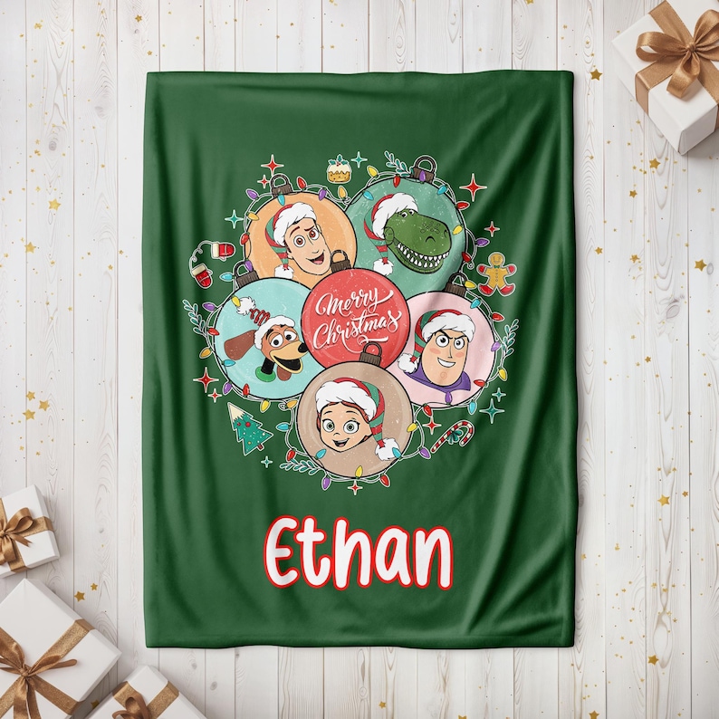 May include: A green Christmas blanket featuring cartoon characters in ornaments, with the text "Merry Christmas" and the name "Ethan" in red. The blanket has a festive design with Christmas lights and ornaments.