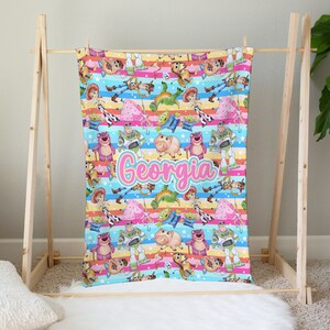 Peut inclure: Une couverture color&eacute;e avec un motif r&eacute;p&eacute;t&eacute; de personnages de la franchise de films Toy Story. La couverture est bleue, rose, jaune et verte avec des rayures blanches. Le nom "Georgia" est &eacute;crit en lettres cursives roses au centre de la couverture.