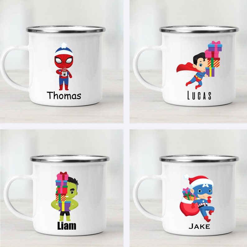 Puede incluir: Cuatro tazas de esmalte blanco con bordes plateados. Cada taza presenta un personaje de superh&eacute;roe diferente sosteniendo regalos. Las tazas est&aacute;n etiquetadas con los nombres "Thomas", "Lucas", "Liam" y "Jake".