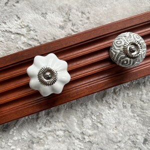 May include: Three ceramic knobs with a white and gray patterned design. The knobs are attached to a wooden surface.