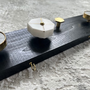 May include: A black wooden board with five decorative hooks. The hooks are made of brass and marble. Two hooks are round, two are hexagonal, and one is a simple hook.