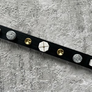 May include: A black wooden board with six decorative knobs. The knobs are made of white marble, gold metal, and a white and gold geometric design. The board is on a gray textured surface.