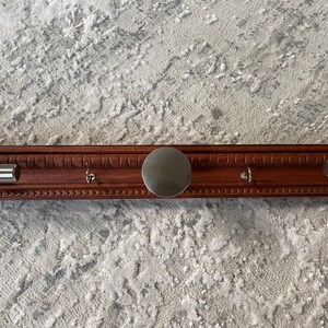 May include: A wooden coat rack with three hooks and a round metal plate in the center. The rack has a dark brown finish and is mounted on a wall.