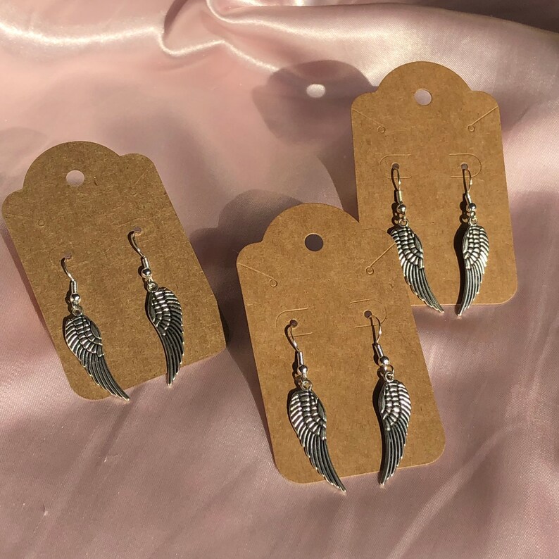 May include: Three pairs of silver angel wing earrings displayed on brown card stock.