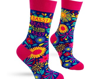 May include: A pair of novelty socks with a vibrant floral pattern in pink, yellow, and blue. The socks feature the text "SASSY BRASSY & a little KISS MY ASSY" on a blue background. The toe and cuff are bright pink.