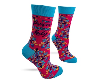 May include: A pair of novelty socks with a vibrant design. The socks are primarily hot pink with a repeating floral pattern in teal, yellow, and blue. The cuffs, heels, and toes are bright blue. Text on the side reads "I'm a Proper Fucking Lady."