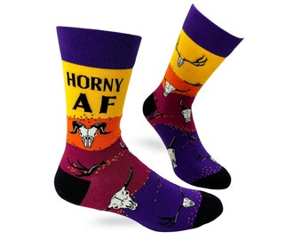 May include: A pair of colorful socks with a skull and antler pattern. The socks have a yellow, orange, red, and purple color gradient. The left sock has the text "HORNY AF" in black letters.