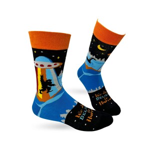 May include: A pair of blue and black socks with a colorful design featuring a UFO, a forest, and the text "We do believe in the hunt".