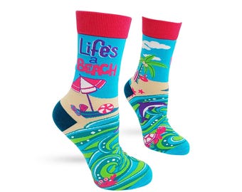May include: A pair of crew socks featuring a bright blue background with a beach scene, including a palm tree, a pink umbrella, a dolphin, a sea turtle, and a red crab. The text "Life's a Beach" is printed in purple and red on the upper section.