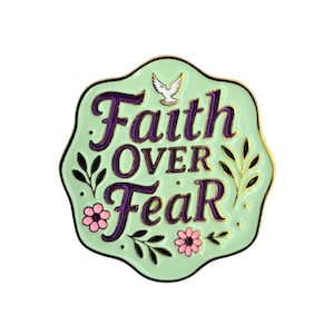 May include: A light green enamel pin with the words "Faith Over Fear" in purple script. The pin features a white dove, pink flowers, and gold accents, set against a white background.