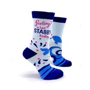 Op de afbeelding: Een paar blauwe en witte sokken met een narwal-afbeelding en de tekst "Feeling a tad stabby today".