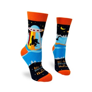 May include: A pair of colorful socks with a blue background and a black and white graphic of a UFO and a monster. The socks have orange cuffs and the text "We do believe in humans" on the bottom.