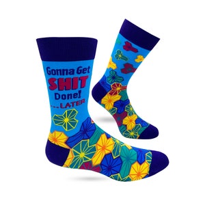 May include: A pair of blue socks with a navy blue cuff and toe. The socks have a geometric pattern in yellow, green, and red. The text "Gonna Get SHIT Done! ...LATER" is printed on the front of one sock.